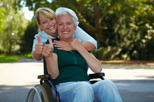Frau im Rollstuhl mit Altenpflegerin aus Polen zeigt Daumen hoch